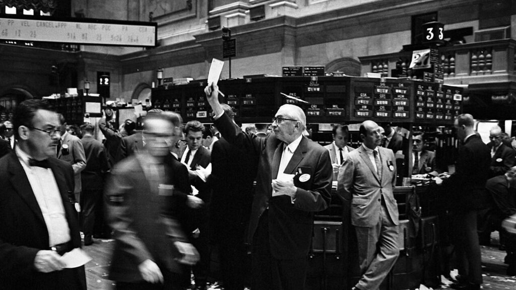 Black and white photo of stock brokers crowding the trading floor of the New York Stock Exchange in 1963